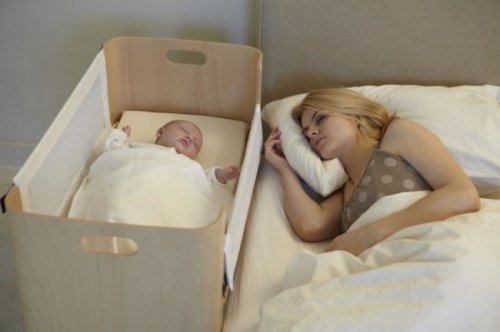 Moeder in bed naast baby in wieg