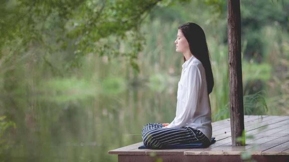 Vrouw zit bij het water te mediteren